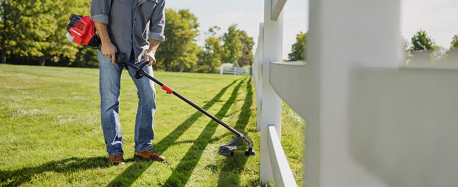 man trimming lawn close to white wooden fence
